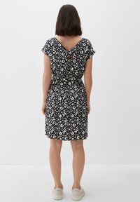 Czarna i biała sukienka w wzory z krótkimi rękawami, tyłem w kształcie litery V i detalem w postaci dziurki. Gładki materiał; długość do połowy uda. Noszona z białymi trampkami.