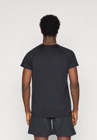 Μαύρο αθλητικό T-shirt με κοντά μανίκια, υφασμάτινη υφή και ράγλεν σχέδιο. Συνδυασμένο με σκούρες βερμούδες, απλός και λειτουργικός σχεδιασμός.