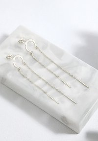 Silberne hängende Ohrringe mit kreisförmigen Ringen, an denen Ketten und gerade Stangenakzente befestigt sind, die auf einer Marmoroberfläche liegen.