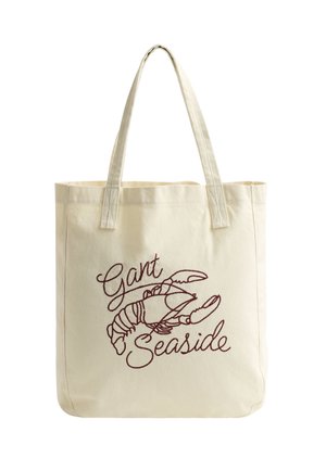 Crèmekleurige draagtas met twee hengsels, afgewerkt met een gestikte afbeelding van een kreeft en de woorden "Gant Seaside" in rode draad.