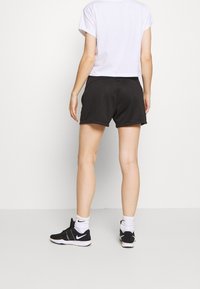 Černé sportovní šortky s hladkou texturou a elastickým pasem, doplněné o zkrácené bílé tričko a černé tenisky.