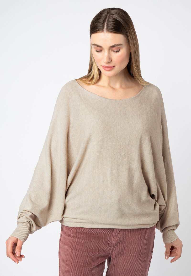 Beige oversized trui met een wijde halslijn, geribbelde manchetten en een zachte textuur. Gecombineerd met roze korduroy broek, die een relaxte pasvorm laat zien.
