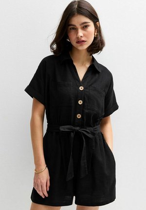Black linen jumpsuit features a collar, short sleeves, wooden buttons, two chest pockets, and a tied waist belt.