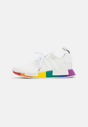 Witte Adidas sneaker met zoolgedeelten in regenboogkleuren, witte veters, zijstrepen en een trekriempje aan de hiel.