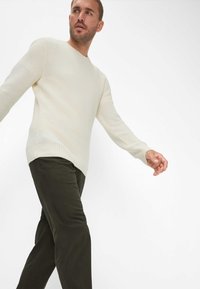 Maglione lavorato a maglia crema con scollatura rotonda, maniche lunghe e finitura testurizzata, abbinato a pantaloni verde scuro.