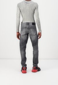 Camisa de manga larga de canalé gris combinada con jeans gris desgastados y zapatillas negras con acentos rojos. Costuras y bolsillos visibles en los jeans.