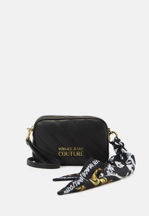 Bolso bandolera acolchado negro de Versace Jeans Couture con logo dorado y pañuelo de tela negro, blanco y dorado con estampado adjunto.