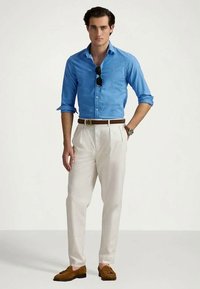 Svetlo modra srajca s prednjimi gumbi, bele plisirane hlače, rjav usnjen pas in svetlo rjavi mokasini iz semiša. Sončna očala počivajo na srajci.