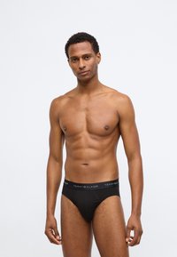 Μαύρο βαμβακερό σλιπάκι με λογότυπο στη ζώνη. Διαθέτει σφιχτή εφαρμογή και λεία υφή, σχεδιασμένο για άνεση και υποστήριξη.