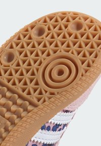 Suela de zapato de goma con superficie texturizada; patrones circulares y hexagonales en color tostado; acentuada con tela rosa y blanca en el borde.