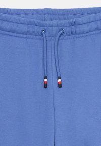 Blå joggebukser med snøring i livet og kontrastfarger i svart, hvitt og rødt på endene. Myk tekstur og elastisk liv for komfort.
