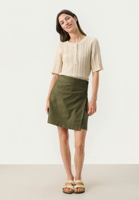 Beige knit short-sleeve top with ribbed texture and three buttons, paired with a knee-length olive green A-line skirt. Simple sandals.