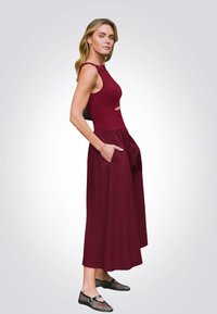 Burgundowa sukienka bez rękawów z wycięciem, zwiewna spódnica i boczne kieszenie. Połączona z czarnymi butami z siateczki z paskiem.