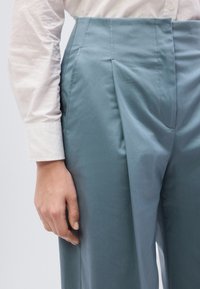 Op maat gemaakte, hooggetailleerde broek in zachte, lichtblauwe stof. Voorzien van plooien en een gladde textuur, gecombineerd met een wit overhemd.