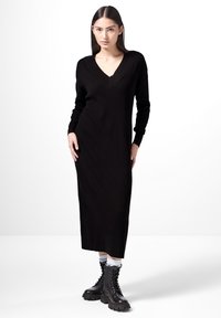 Robe midi en tricot noir côtelé avec un décolleté en V et des manches longues ; associée à des bottes de combat à lacets noires et des chaussettes blanches. Texture lisse.