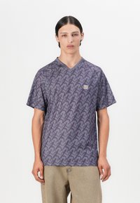 Sivá tričko s krátkym rukávom a véčkovým výstrihom, s opakujúcim sa tmavosivým abstraktným vzorom a malým zeleným logom na hrudi.