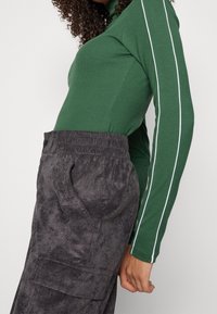 Grön ribbad långärmad tröja med vita sidosträck som är ihop med mörkgrå strukturerade byxor med elastiskt midjeband och sidofickor.