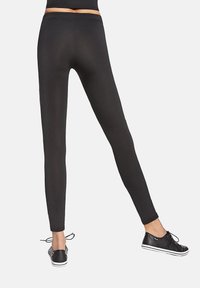 Czarne legginsy o gładkim wykończeniu, z wysokim stanem i dopasowanym krojem, zestawione z czarnymi trampkami z białymi podeszwami.