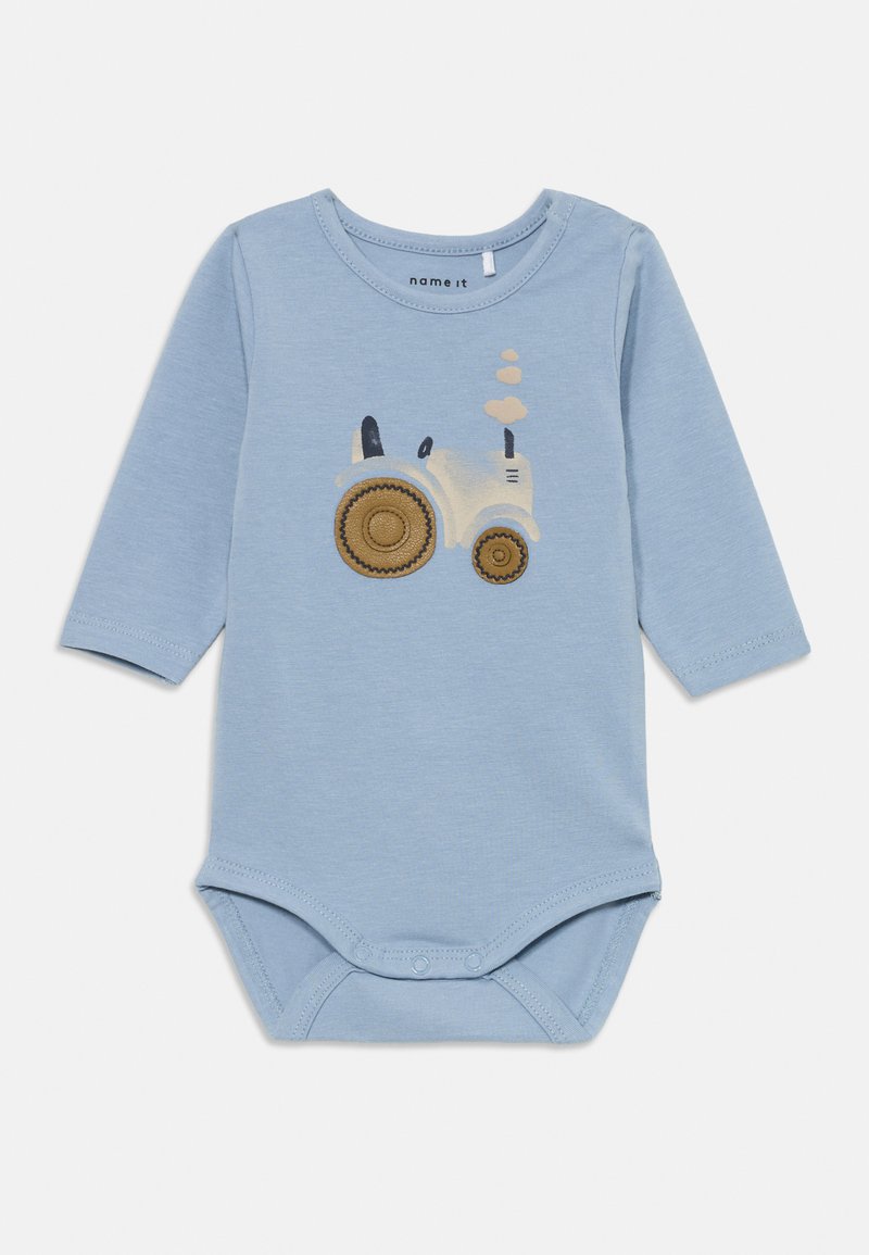 Lichtblauwe longsleeve rompert met een tractorafbeelding in wit en bruin, met drukknoopsluitingen aan de onderkant en een ronde halslijn.
