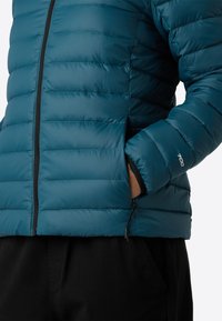 Giacca blu trapuntata con zip frontale e mano nella tasca laterale con zip, indossata su pantaloni neri. "700" ricamato sulla manica.