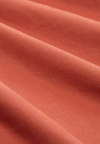 Tissu en coton de couleur corail atténuée avec une texture lisse, présentant des plis diagonaux et un motif de tissage uniforme.