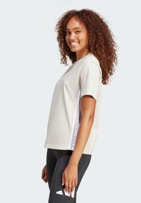 Helles beige T-Shirt mit kurzen Ärmeln und einem lässigen Schnitt sowie weißen Seitenstreifen. Hergestellt aus weichem Material, mit einem Rundhalsausschnitt.