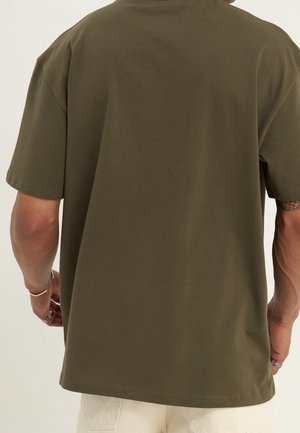 Olivově zelené bavlněné tričko s volným střihem, krátkými rukávy a kulatým výstřihem. Jednoduchá, jednotná textura s rovnými lemy.