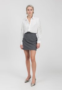 Blusa di raso bianca con maniche ricamate, abbinata a una mini gonna grigia a pois. Completata da tacchi alti con stampa pitone.