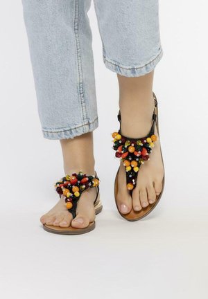 Sandales thong noires avec des accents de perles multicolores sur la sangle supérieure, semelle beige et semelle plate. Portées avec un pantalon en denim court clair.