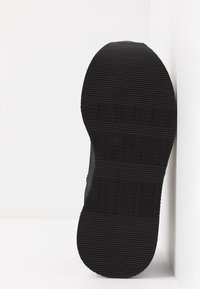 Czarna podeszwa sneakersów z teksturowaną gumową powierzchnią w zygzakowaty wzór oraz wytłoczonym logo "NONAME" na całej powierzchni.