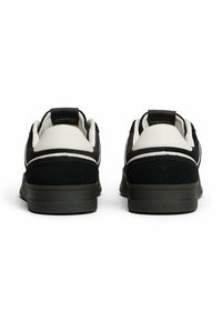Para czarno-białych niskich trampków z grubymi podeszwami, widziana z tyłu, z logo "TOMMY JEANS" na podeszwie.