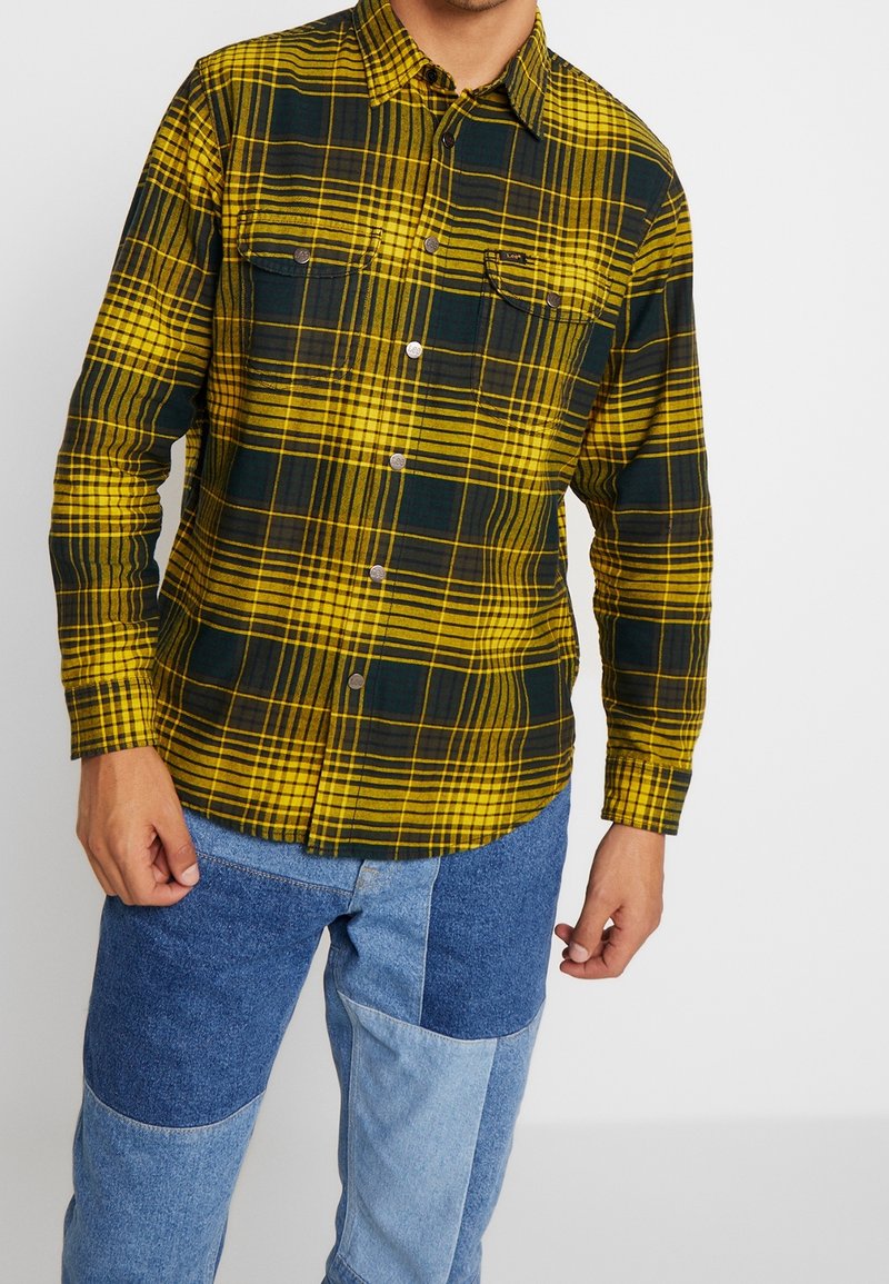Geel en donkergroen geblokt flanellen overhemd met knoopsluiting, twee borstzakken en een afgeronde zoom, gecombineerd met patchwork spijkerbroek.
