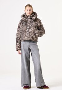 Veste matelassée à imprimé léopard avec un col montant, des manches longues et un design court, associée à un jean gris à jambe large et des chaussures bordeaux.