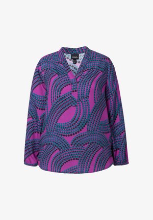 Koszulka z dekoltem w kształcie V, z długim rękawem, w fioletowym materiale z wzorem w turkusowe i czarne kropki. Posiada luźny krój i lekko zaokrąglony dół.