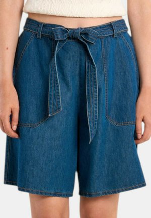 Denimshorts med forlommelommer og et bundet stofbælte, båret med en lysefarvet tekstureret top.