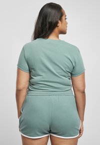 Lys grønn bomull T-skjorte med korte ermer, kombinert med matchende shorts med hvite detaljer. Synlig ryggdetalj og jevn tekstur.