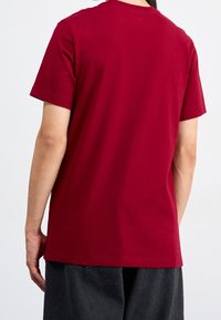 Bordowa bawełniana koszulka z krótkimi rękawami, okrągłym dekoltem i prostym wzorem. Miękka, gładka w dotyku, o regularnym kroju.