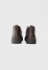 Botas de tobillo de cuero marrón con un acabado texturizado, que presentan un diseño elegante y suela de goma negra. Letra de la marca en el talón.