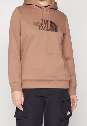 Bruine The North Face-hoodie met voorzak, gedragen met zwarte cargobroek met logo op de zak.