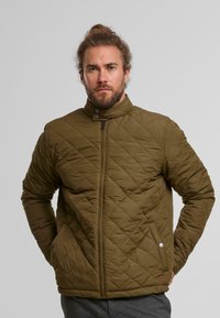 Vihreä, vuorattu takki, jossa on korkea kaulus, vetoketjusuljenta ja napitustaskut. Ominaisuuksiin kuuluu timanttikuosi ja teksturoitu kangas.