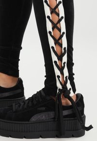 Sammetssvarta leggings har vit snörningsdetalj längs sidorna. Kombineras med svarta platåskor i mocka.