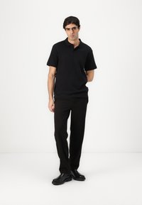 Zwarte polo met korte mouwen, relaxte pasvorm, gecombineerd met zwarte rechtlijnige broeken en zwarte schoenen. Soepele textuur, minimalistisch ontwerp.