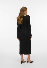 Melna ribota ad�īta kleita ar garām piedurknēm un taisnu siluetu, kurai ir šķēlums apakšmalā, un to valkā ar brūniem papēžu zābakiem.