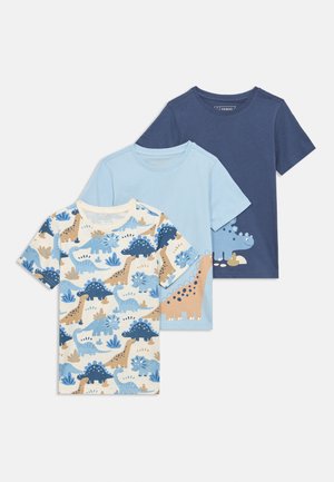 Tre magliette a maniche corte per bambini: una blu navy con grafica di dinosauro, una azzurro chiaro con grande dinosauro e una bianca con stampa di dinosauri su tutta la superficie.