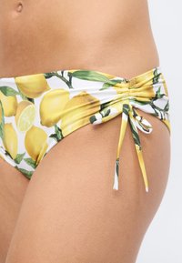 Κοντινό πλάνο ενός προσώπου που φοράει μαγιό με μοτίβο λεμονιών, με ρυτιδώσεις στα πλάγια και δεμένα κορδόνια σε φωτεινό δέρμα.