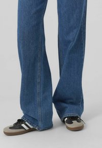 Jeans din denim albastru cu croială evazată, având o nuanță medie. Asortați cu teniși negri și gri cu dungi albe.