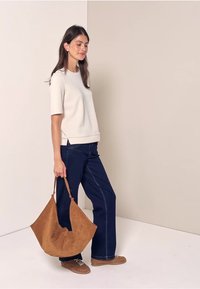 Cremefarvet kortærmet top med lige pasform, parret med mørkeblå denim brede bukser og en brun ruskinds tote taske. Brune sneakers.