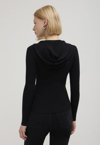 Figurbetonter schwarzer Rippstrickpullover mit Kapuze, langen Ärmeln und abgerundetem Saum, der eine weiche Textur und minimalistische Nahtdetails präsentiert.
