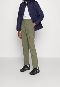 Granatowa pikowana kurtka, biała koszulka, oliwkowe spodnie cargo z kieszeniami i czarne buty sportowe. Skupienie na funkcjonalnej odzieży na świeżym powietrzu.