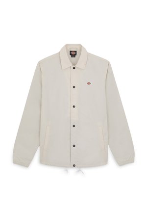 Chaqueta ligera beige con cuello de solapa, cierre frontal de botones, dos bolsillos laterales y un pequeño logotipo en el lado izquierdo del pecho.